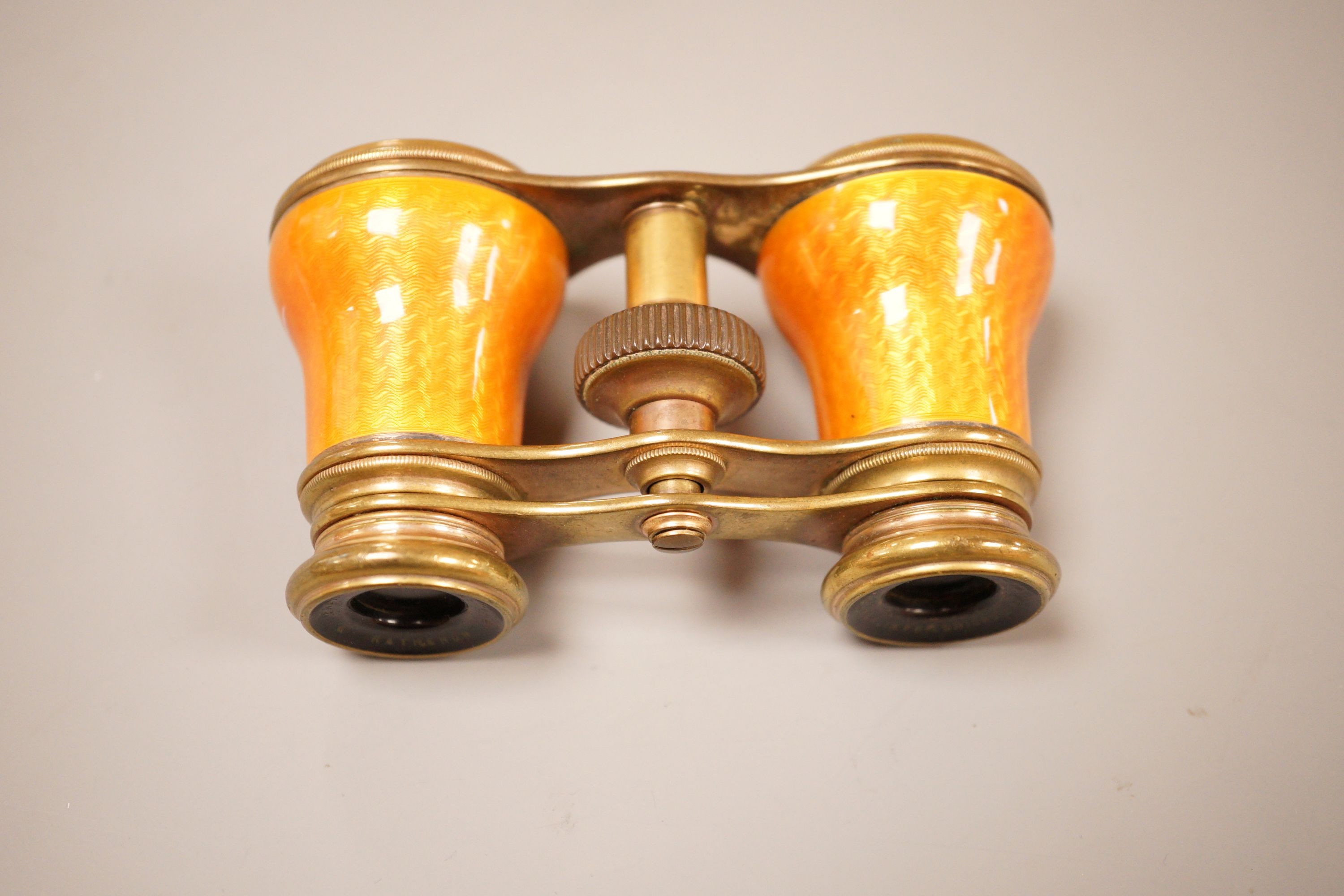 A pair of German orange enamelled opera glasses, inscribed Fabr Emil Busch, Rathenow to the left lens, and E. Petitpierre, BerlinFriedrichstr. to the right lens, 10cm wide